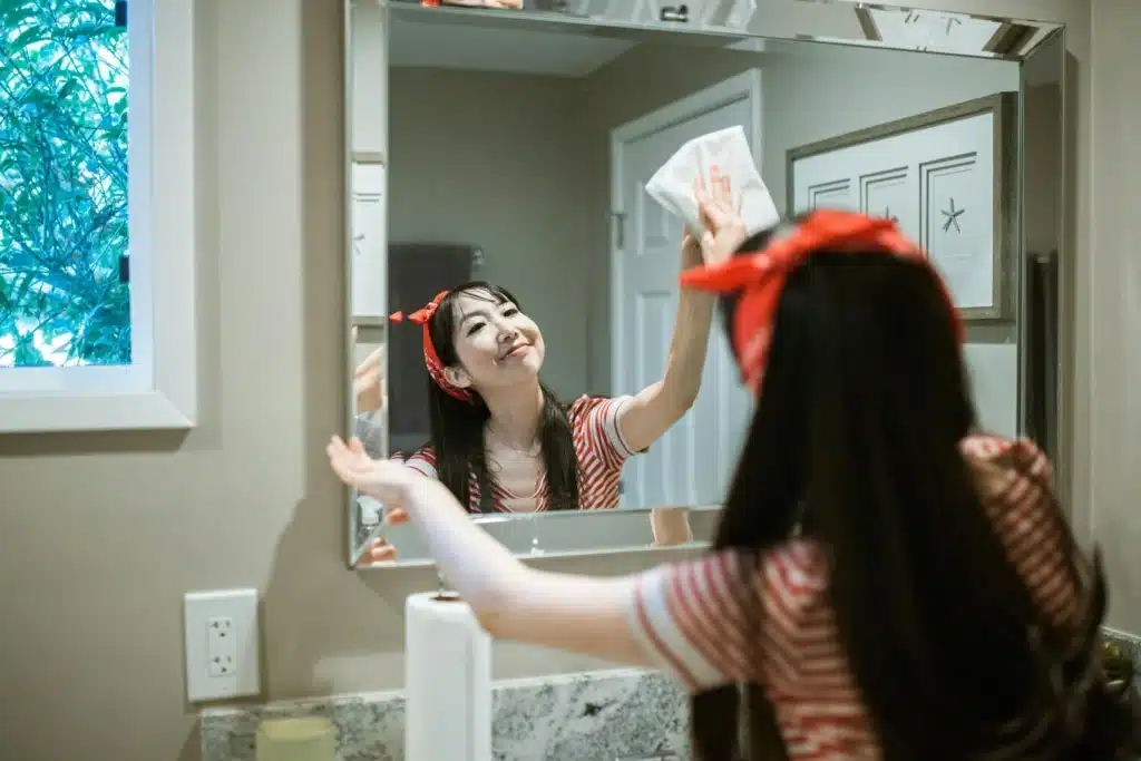 Happy house cleaner wiping down a bathroom mirror with a cloth