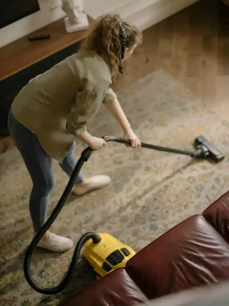 Someone cleaning a patterned rug with a vacuum in a comfy living room.