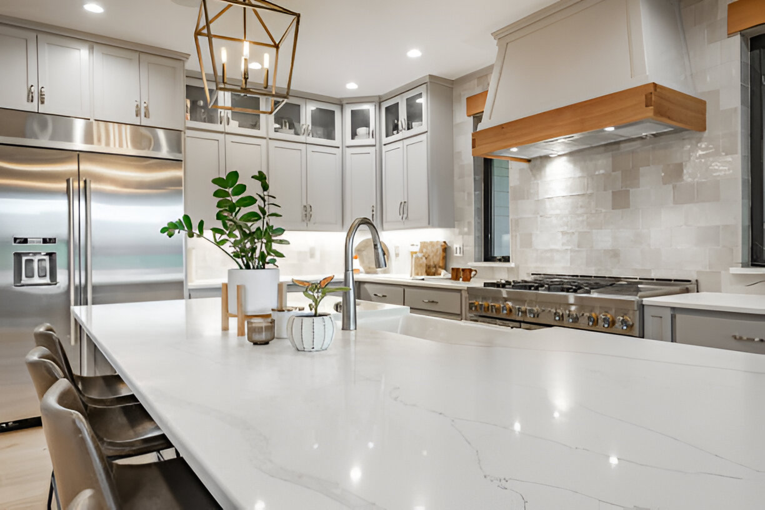 Modern kitchen with stainless steel appliances, sleek white countertops, a hanging light fixture, plants on the island, and stylish cabinetry, showcasing a clean and elegant design.